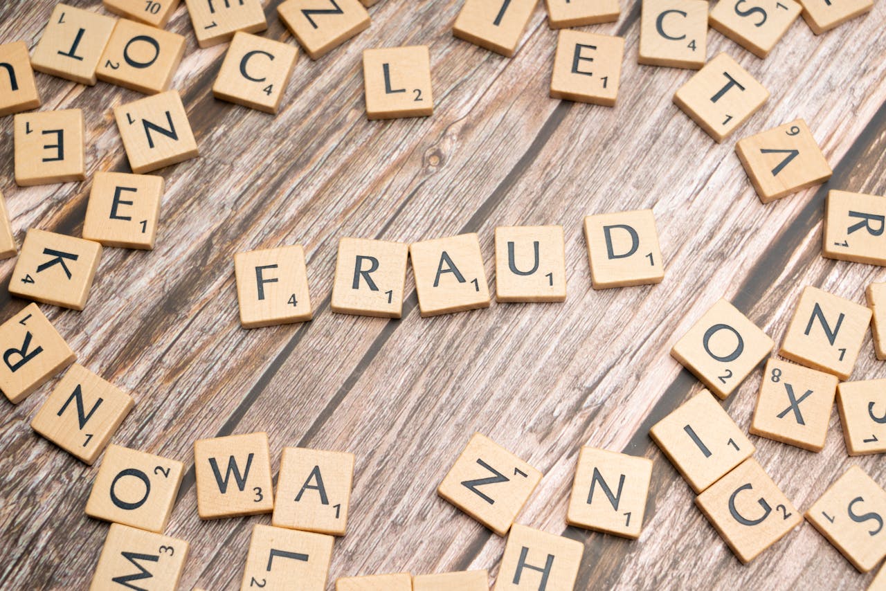 Alphabet tiles arranged to spell 'fraud' on a wooden surface, symbolizing deception.